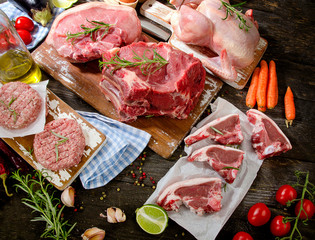 Different types of fresh raw meat with herbs on wooden table.
