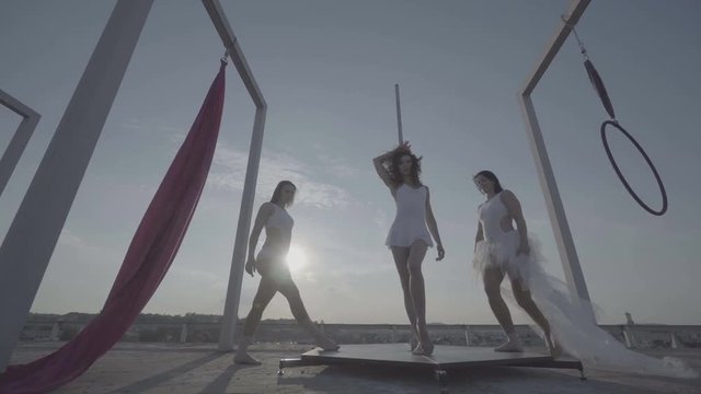Three beautiful sexy girl performing acrobatic stunts on the roof at sunset.