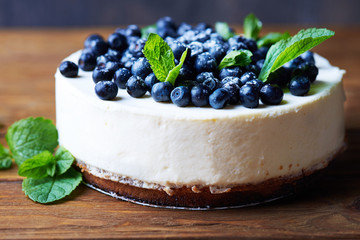 Close view at sweet creamy blueberry cheesecake with fresh blueberries and mint leaves on a wooden background with copy space.