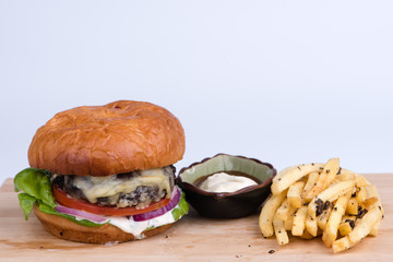 Cheeseburger with french fries and dips on wooden board, white b