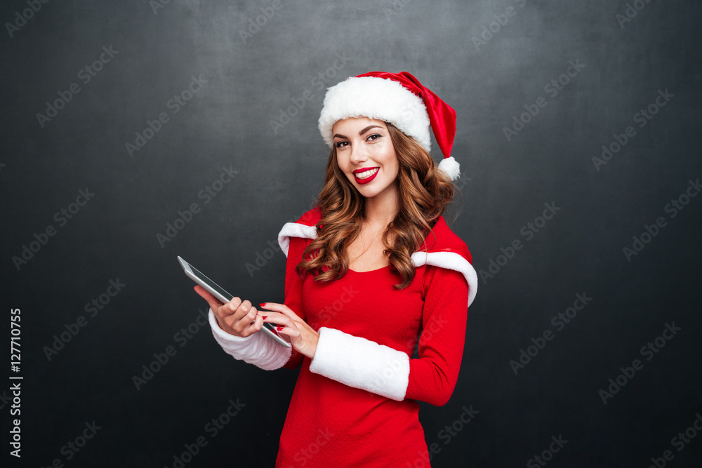 Poster Happy woman in santa claus costume standing and using tablet