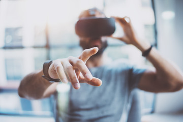 Closeup of male hand.Bearded young man wearing virtual reality goggles in modern coworking studio. Smartphone using with VR headset in office. Horizontal, blurred.