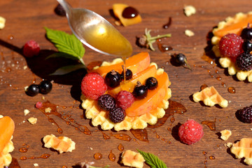 Honey flowing down from spoon on waffle with fruits and berries  