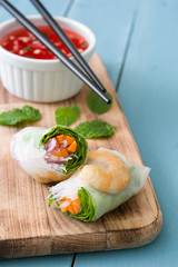 Vietnamese rolls with vegetables, rice noodles and prawns on blue wooden background
