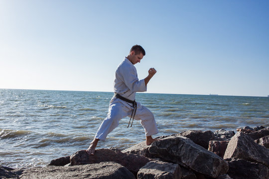 image of male karate fighter posing on stones sea background
