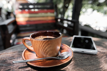 A cup of coffee and smart phone on a wooden table.