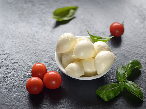 Top view of mozzarella cheese with cherry tomatoes and basil on a black slate surface
