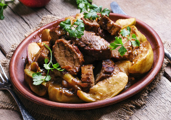 Pork stew with apple sauce, vintage wooden background, selective