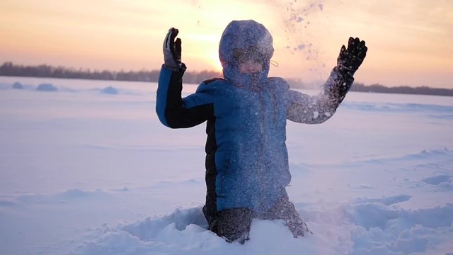 g child throwing snow over himself and enjoys it in winter park at sunset