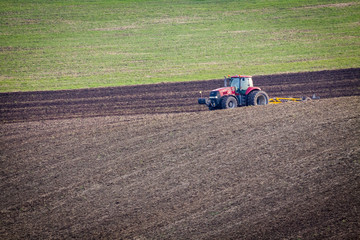 Red tractor plows the field in autumn.