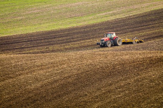 Red tractor plows the field in autumn.
