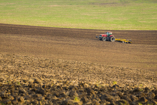 Red tractor plows the field in autumn.