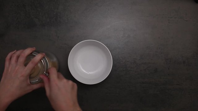 Young woman measures out brown sugar into a white bowl on a counter-top