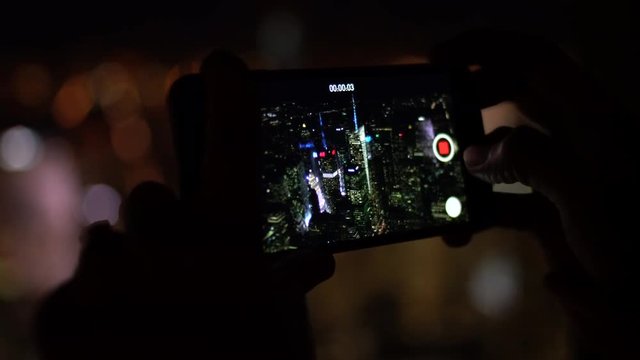 New York skyline filmed on a smart phone at night by a young woman, city lights out of focus in the background