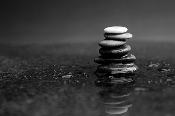 Pebble stack in black and white with black pebbles and one white on the top lying on wet marble 