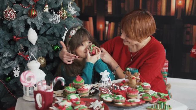 Mother and her kids playing with christmas cakes and candies near dressed up tree