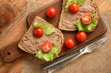 Chicken liver pate on the bread on wooden tray.