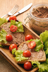 Chicken liver pate on the bread on wooden tray.