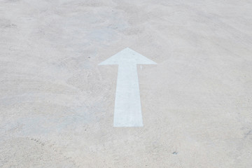 Closeup white painted arrow sign on cement street floor textured background