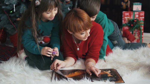 Mother with her kids reading the book near dressed up christmas tree