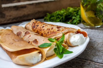 Russian thin pancakes with butter, cheese, jam, mint tea with lemon on a napkin on a wooden background.  Love for a healthy sweet  food concept