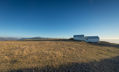 Fototapeta premium Lonely house on grass hill with blue sky in southern Iceland