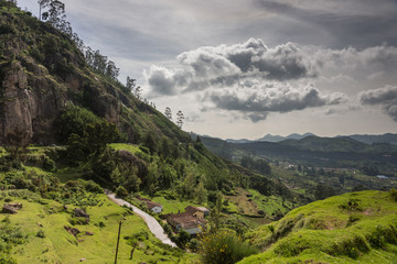 Ooty, India - October 25, 2013: Panoramic scenery of the Nilgiri hills shows forest, many hills at horizon, free floating stormy clouds, rocks, a road and a farm. Shades of green. Shot from us a hill.