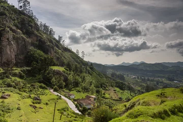 Fototapeten Ooty, India - October 25, 2013: Panoramic scenery of the Nilgiri hills shows forest, many hills at horizon, free floating stormy clouds, rocks, a road and a farm. Shades of green. Shot from us a hill. © Klodien