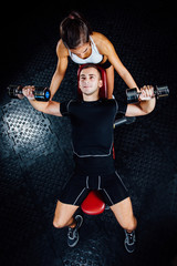 Female personal fitness instructor helping a young man at gym.