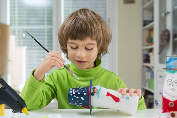 Little boy being creative making homemade do-it-yourself toys out of yogurt bottle and paper. Supporting creativity, learning by doing, hand craft. Creative leisure for children indoors.