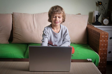 Little boy amused watching something funny on laptop.