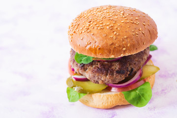 Big sandwich - hamburger burger with beef, pickles, tomato and red onions on a light background.