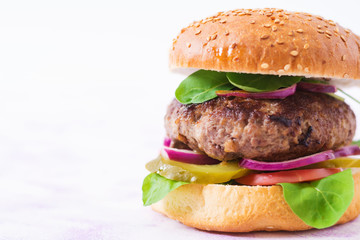 Big sandwich - hamburger burger with beef, pickles, tomato and red onions on a light background.