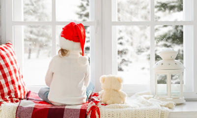 Fototapeta premium happy child girl sitting back in winter window Christmas