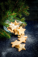 Traditional Christmas gingerbread cookies in the jar near Christmas tree branches, pine cones and decoration. On a dark blue wooden table, sprinkled with powdered sugar or artificial snow