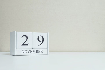 Closeup white wooden calendar with black 29 november word on blurred white wood desk and cream color wallpaper in room textured background with copy space , selective focus at the calendar