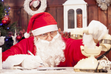 santa claus on the phone at his home compiles the wishlist for c