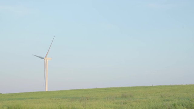 Looking across a field at a wind turbine turning, generating electricity. Blue sky background. Space for copy.
