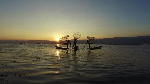 Inle Lake fishermen in Myanmar are posing with traditional nets for tourists at sunset.