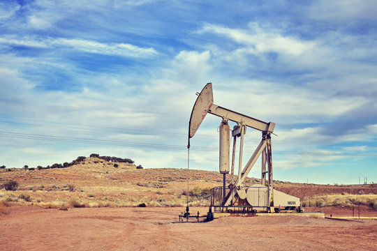 Retro toned picture of an oil pump, old industrial equipment on arid soil.