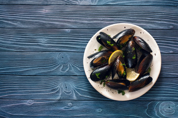 Mussels on white plate over blue wood background