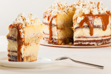 Homemade cake with hazelnuts and salty caramel with vanilla - hazel shortcakes and delicate hazelnut cream, decorated with salty popcorn. Cut a piece of cake on a plate.