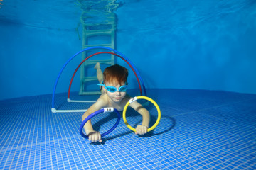 Baby training underwater in the pool and swims through hoops. The view from under the water. Landscape orientation