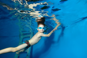 The child learns to swim underwater, holding coach's hands and looks at me. The view from under the...