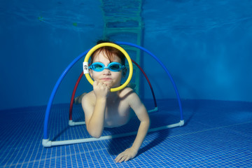 The child swims and trains under the water, lying on the bottom of the pool and looks through the ring. Close-up. The view underwater. Landscape orientation © alexbard
