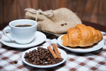 black coffee with beans and croissant on tablecloth