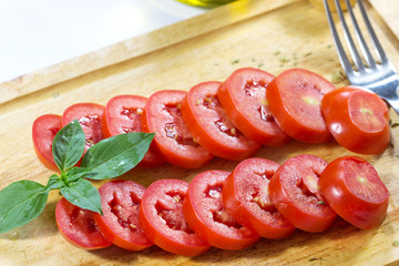 Sliced tomatoes on a wooden cutting board with olive oil and Oregano And green basil on white background / Fresh tomatoes on a wooden cutting board on white background