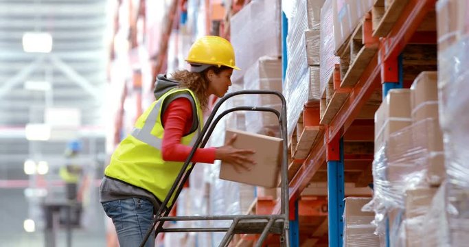 Male warehouse worker using ladder to arrange cardboard box
