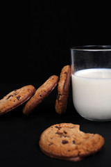 Chocolate chip cookies and glass of milk on black background