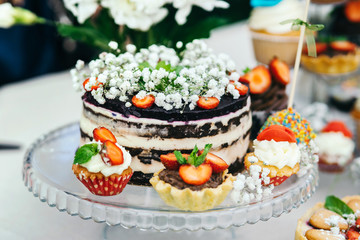 The cake is decorated with white flowers and strawberries cottage cheese cream. Arranged around the cupcakes.